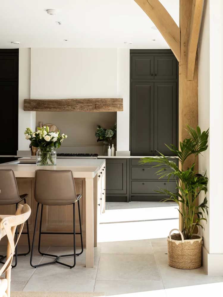 Kitchen with dark green cabinets, a pale oak island with leather stools and an exposed oak frame post